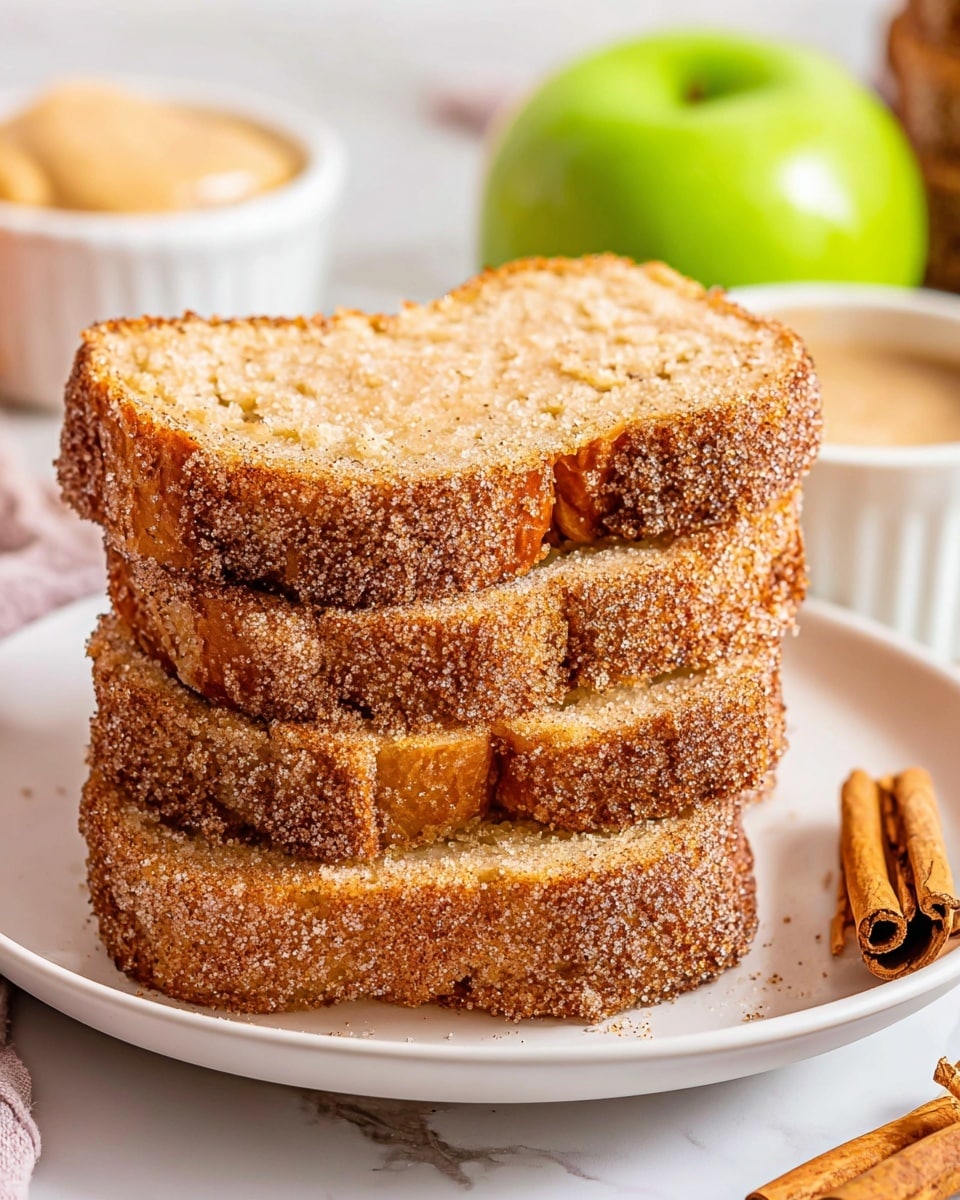 A stack of three thick slices of golden brown cinnamon sugar bread placed on a white plate, showing a soft, crumbly texture inside with a sugary, slightly crispy crust covered in granulated sugar. The slices are uneven but neatly stacked, and on the side of the plate are two cinnamon sticks. In the background on a white marbled surface, part of the rest of the loaf is visible, along with a green apple and a small white bowl with a light beige spread. Photo taken with an iphone --ar 4:5 --v 7