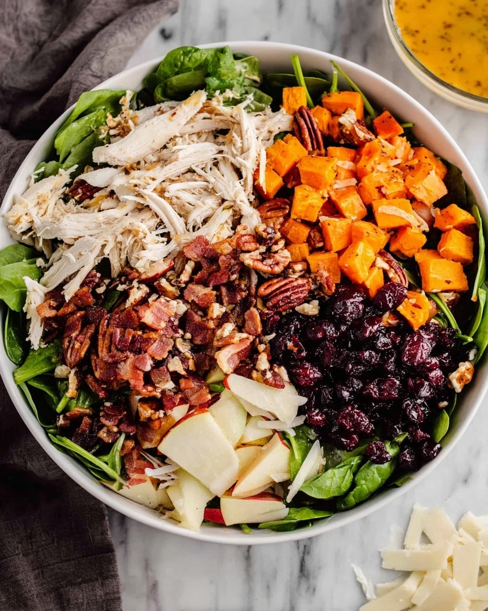 A white bowl filled with a colorful salad arranged in separate layers. The base is fresh dark green spinach leaves, topped with a layer of shredded white chicken in the middle. Above and around the chicken, there are crispy brown bacon pieces, deep red chopped apples with white inside, and dark brown pecans. On one side, there are bright orange roasted sweet potato cubes, next to a small pile of dark purple dried cranberries. White shaved cheese pieces are placed in two separate spots near the edge. In the background, part of a white bowl with orange salad dressing and a white marbled surface are visible. Photo taken with an iphone --ar 4:5 --v 7