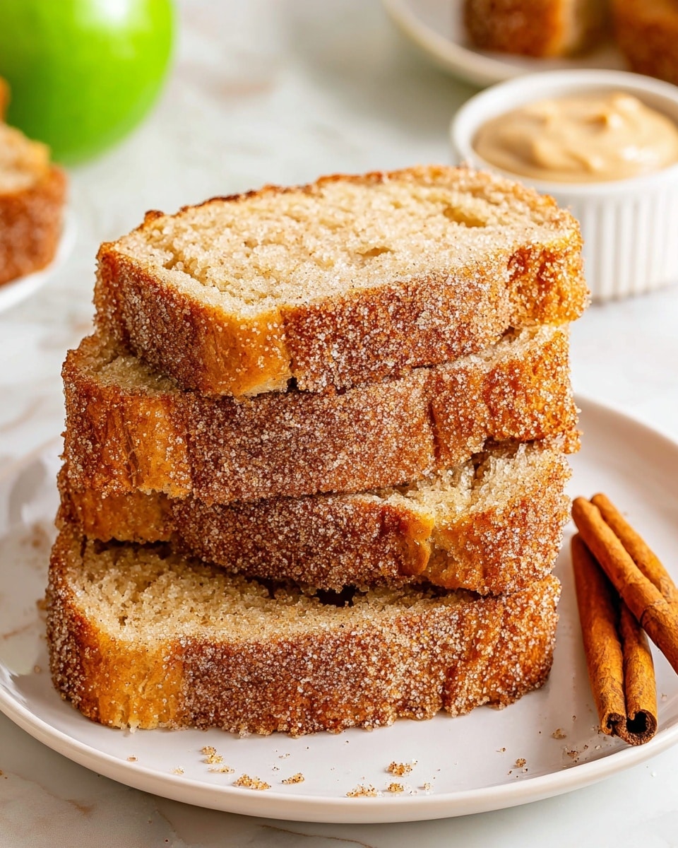 A stack of three thick slices of cinnamon sugar-coated bread is placed on a white plate. Each slice has a golden brown crust with a rough, sugary texture, while the inside is soft and light tan. To the right of the plate are two cinnamon sticks resting on the white marbled surface. In the background, a green apple and a white ramekin with a creamy beige spread are softly blurred. Photo taken with an iphone --ar 4:5 --v 7