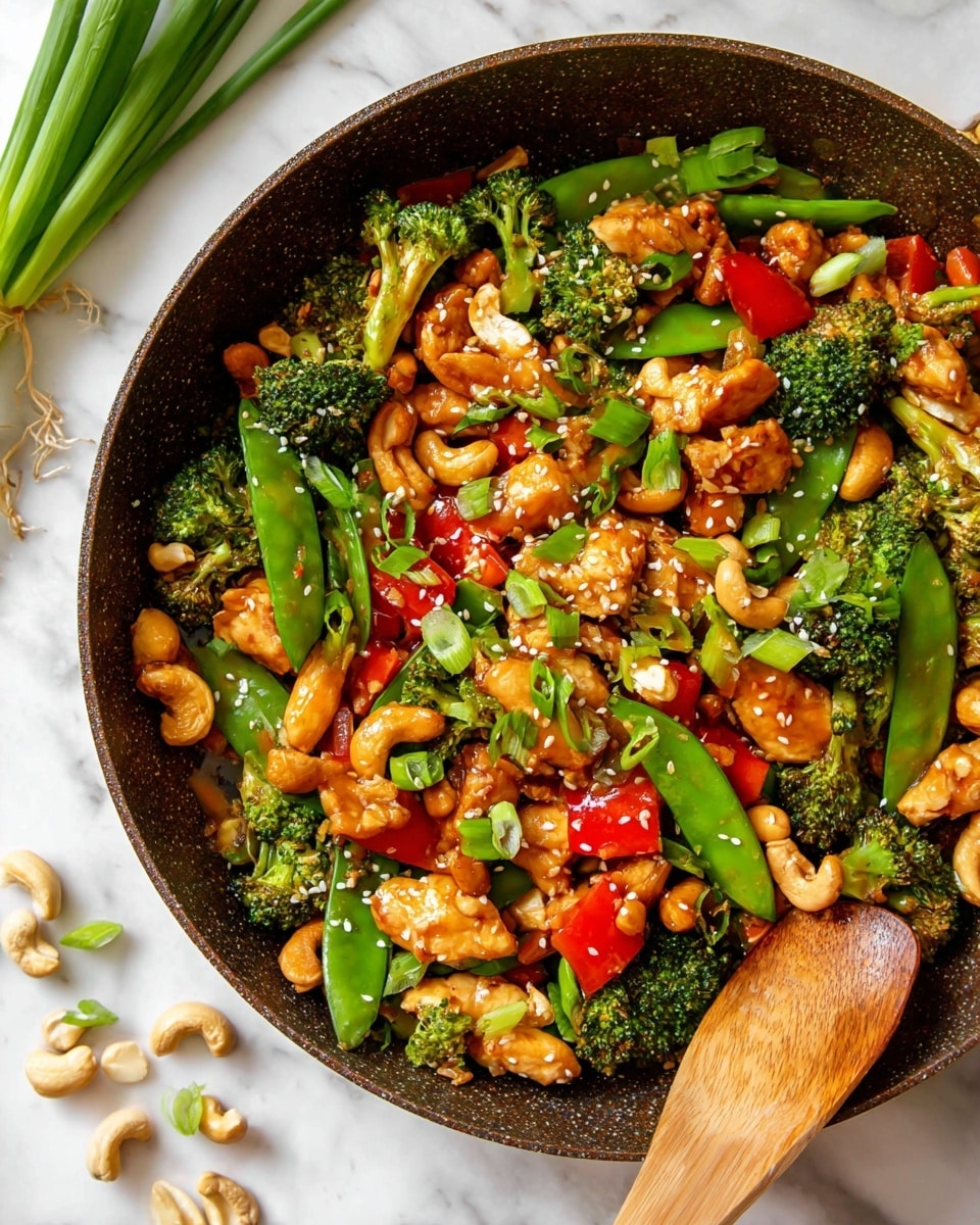 A close-up top view of a cooked stir-fry dish in a large round pan with a wooden spoon on the right side. The dish has multiple colorful layers: green broccoli florets and snap peas, orange-red bell pepper chunks, light golden-brown pieces of chicken, and roasted brown cashews. The ingredients are coated in a glossy sauce with a sprinkling of sesame seeds and chopped green onion on top. Around the pan on a white marbled surface are some loose cashew nuts and green onion stalks placed diagonally in the top left corner. photo taken with an iphone --ar 4:5 --v 7