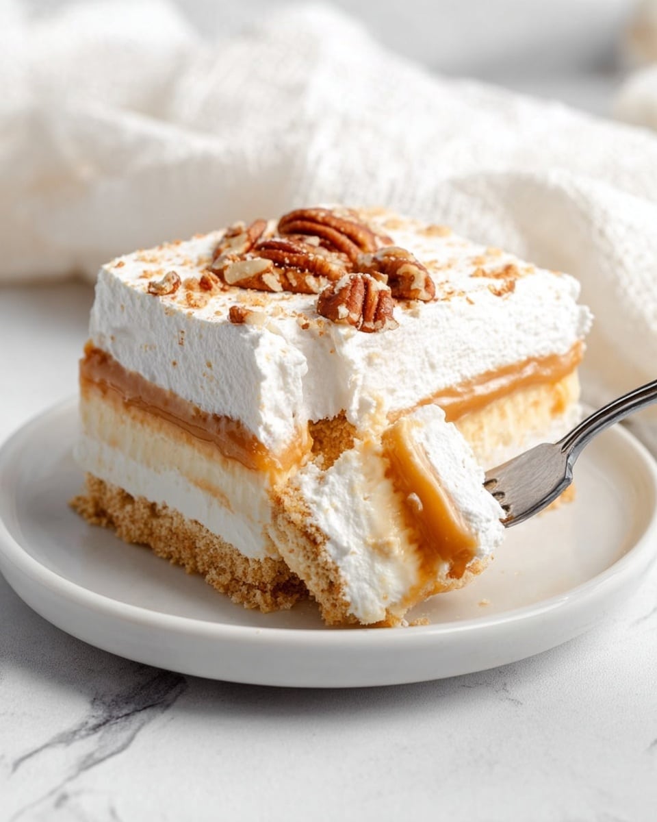 A square slice of layered dessert sits on a white plate placed on a white marbled surface. The dessert has four distinct layers: a crumbly light brown base, a thick creamy white layer above it, a smooth tan caramel-colored layer next, and a thick fluffy white topping sprinkled with pieces of pecans on top. A silver fork is cutting into the slice from the right side, holding a bite-sized portion of the whipped top and caramel layer. A white cloth is softly draped in the background. photo taken with an iphone --ar 4:5 --v 7