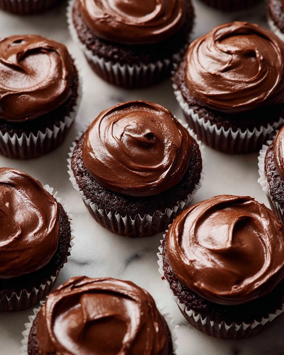 The image shows a close-up of nine chocolate cupcakes arranged closely together on a white marbled surface. Each cupcake has one thick layer of dark chocolate cake topped with a smooth, glossy, dark brown chocolate frosting layer that is swirled in a circular pattern. The cupcakes sit in white paper liners with ruffled edges. The frosting has a rich, creamy texture, catching the light to show its glossy finish. The overall look is dense, moist, and very chocolaty. photo taken with an iphone --ar 4:5 --v 7