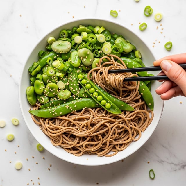 A white bowl filled with three layers of food sits on a white marbled surface. The first layer is brown soba noodles with a shiny, slightly wet texture that are twisted and coiled in the bowl. The second layer is bright green broad beans and snap peas, some snap peas are cut open showing small peas inside. The third layer is sliced green onions scattered on top and around the bowl, adding a fresh look. A woman's hand holding dark chopsticks is picking up some noodles and vegetables from the right side of the bowl. Small sesame seeds are sprinkled over the food and scattered on the surface around the bowl. Photo taken with an iphone --ar 4:5 --v 7