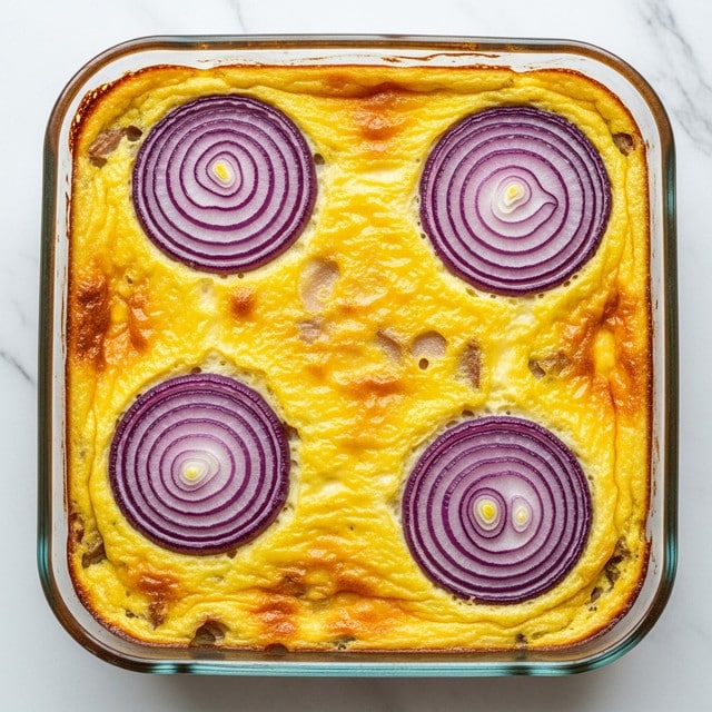 A baked casserole dish with a golden yellow baked egg layer covering the top, slightly browned at the edges. On top are four round slices of purple-red onion, each with clear concentric rings, spaced apart across the surface. The casserole is in a clear glass square baking dish placed on a white marbled surface. The texture of the baked layer looks soft with small chunks visible underneath, suggesting ingredients mixed in. Photo taken with an iphone --ar 4:5 --v 7